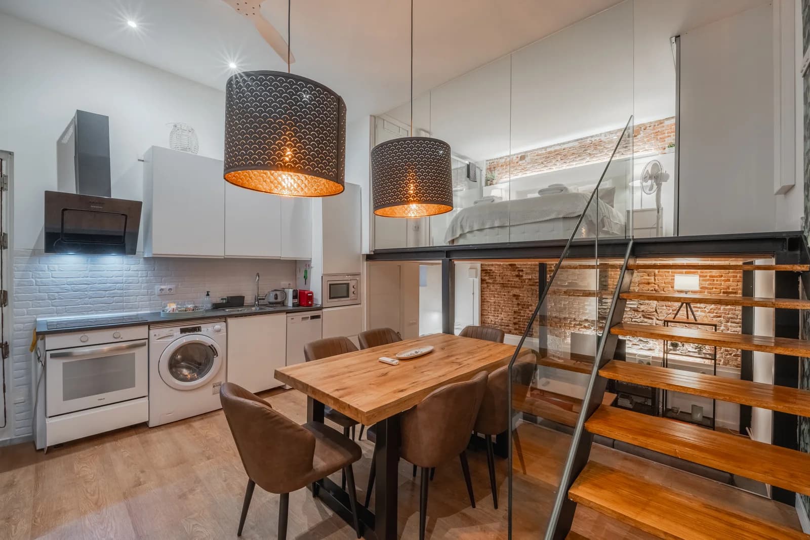 Compact kitchen with rattan pendants, oak table and steel staircase