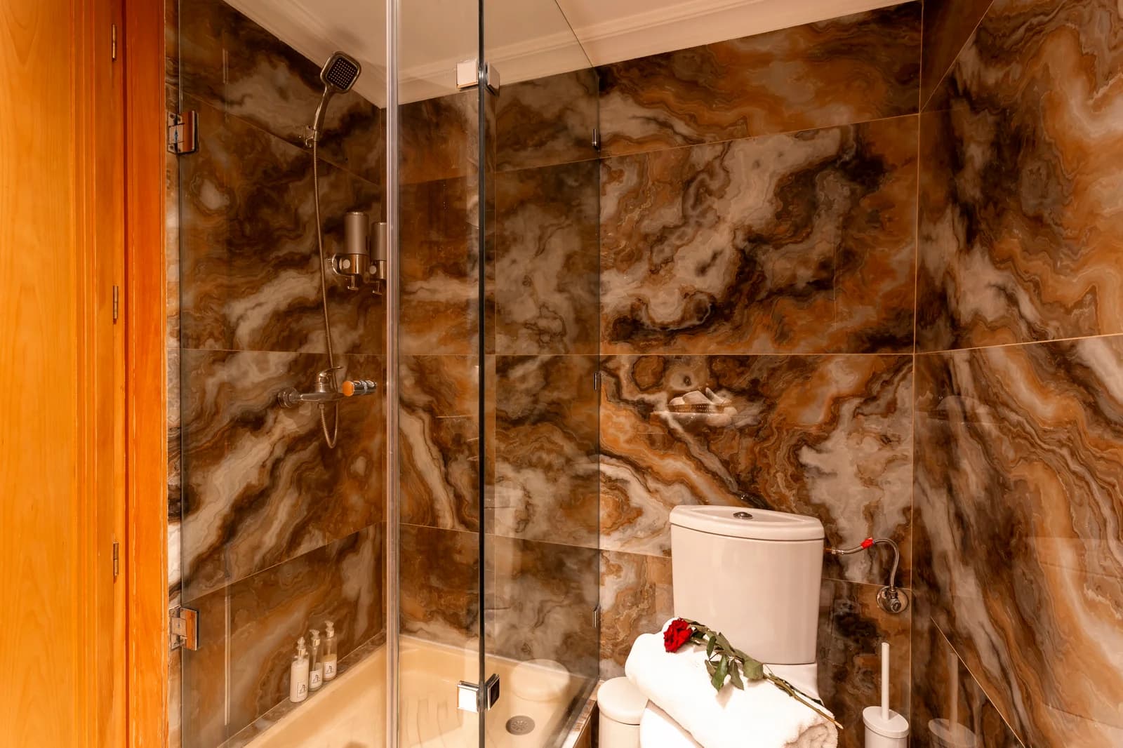 Onyx-veined shower with single rose laid on the toilet rim