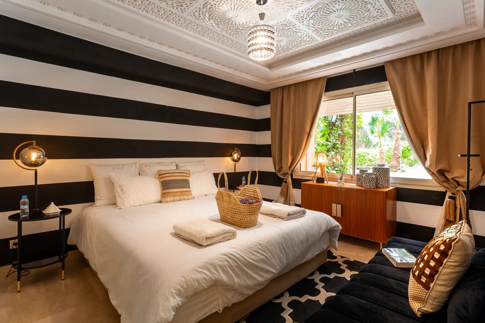 Striped bedroom with carved Moroccan ceiling and palm-filtered light