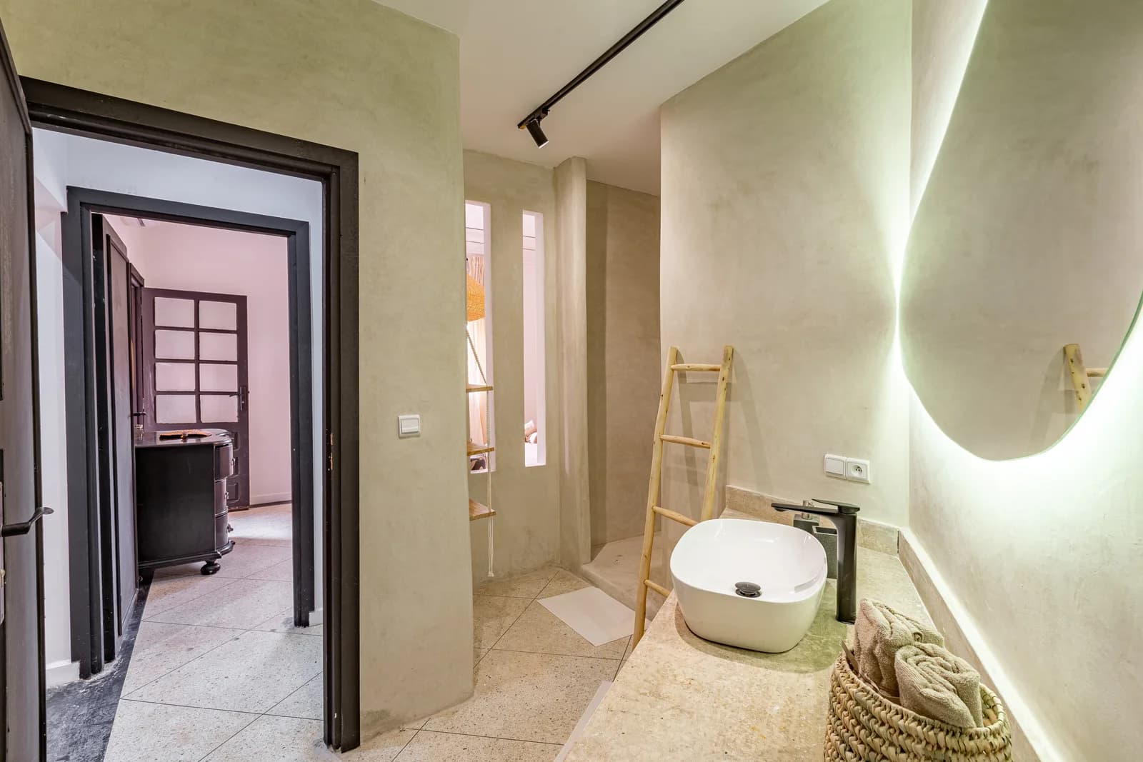 Sage tadelakt bathroom with backlit organic mirror and wooden ladder