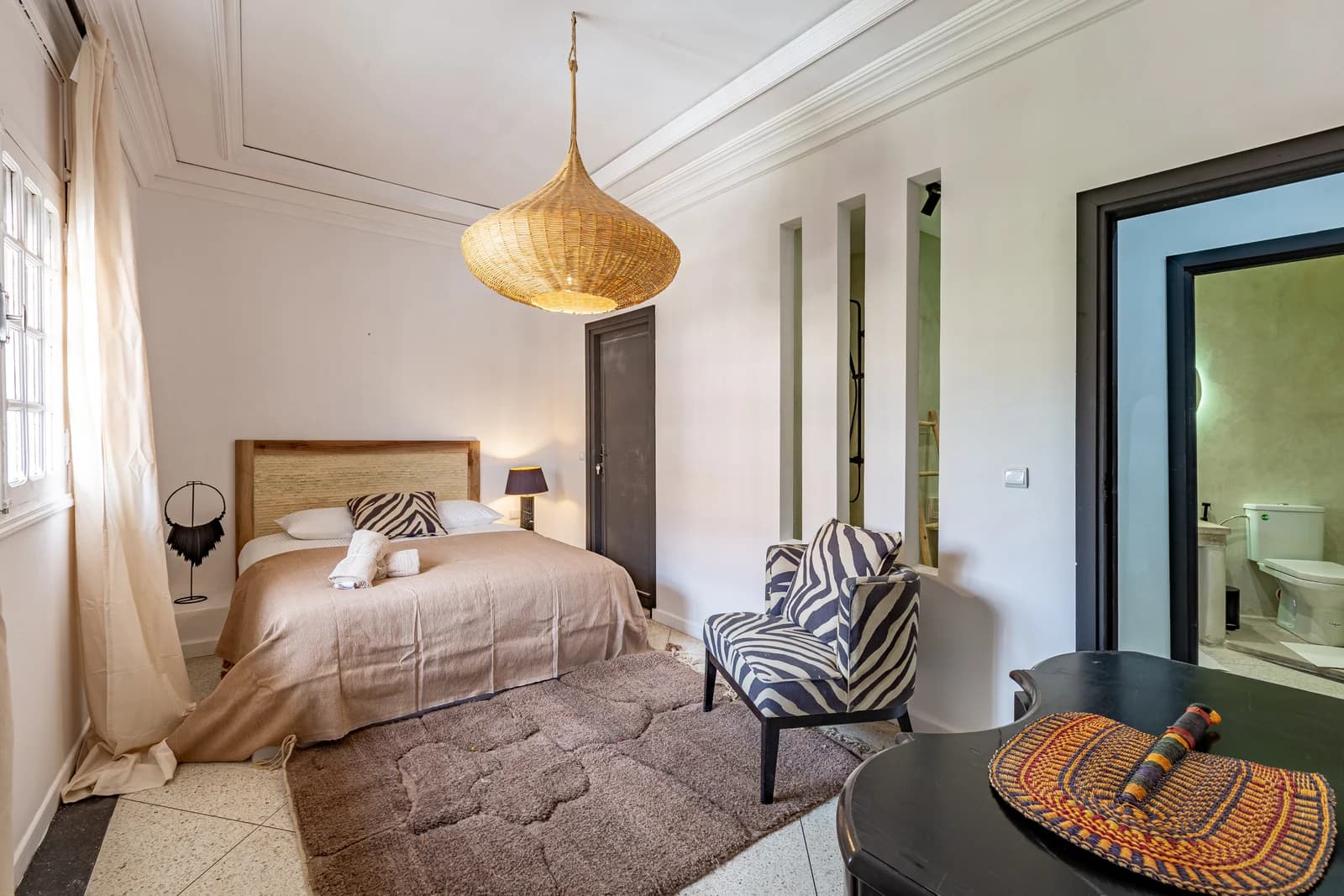 Soft-lit bedroom with rattan pendant and zebra accent chair