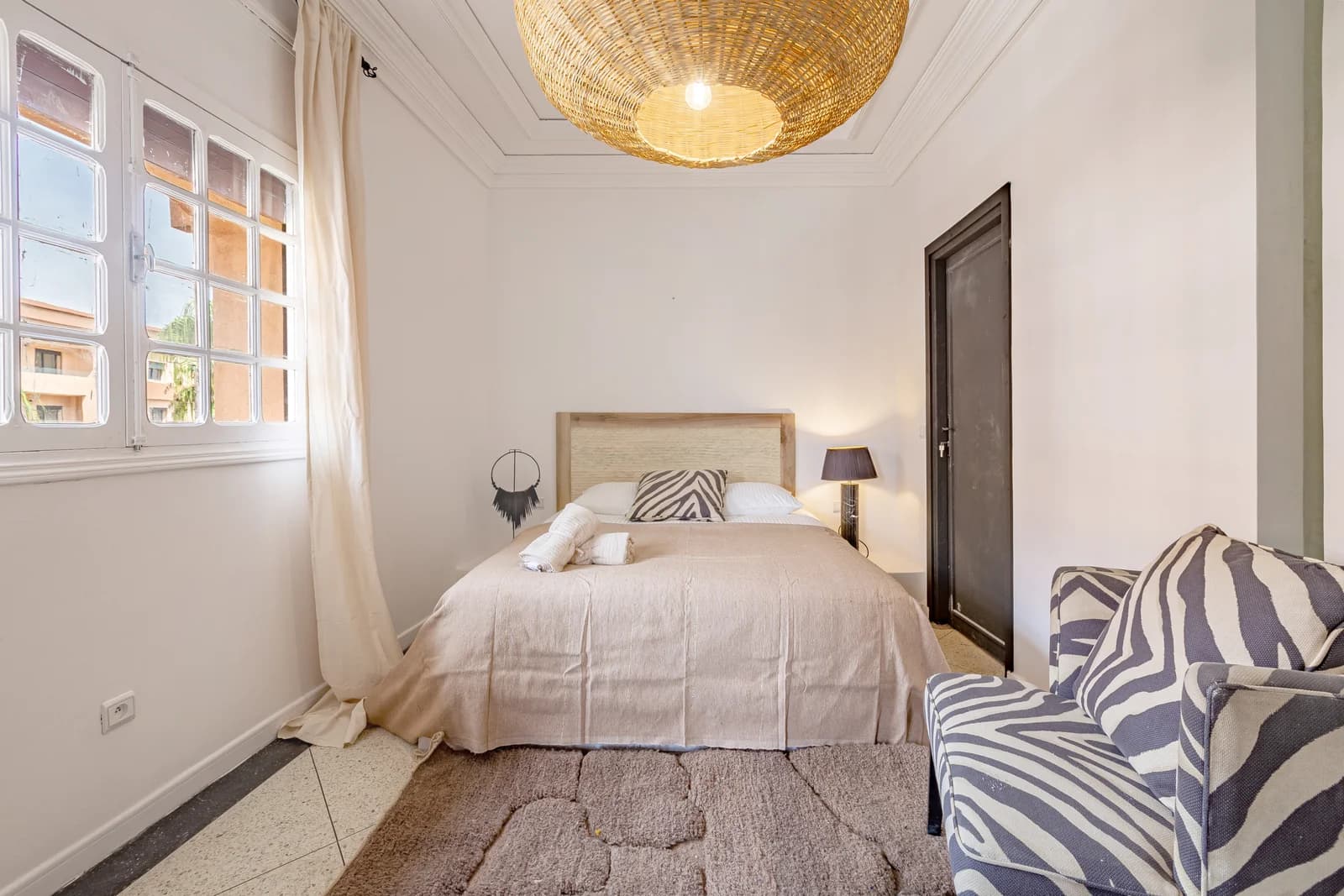 Sun-washed bedroom with woven rattan pendant and zebra chair